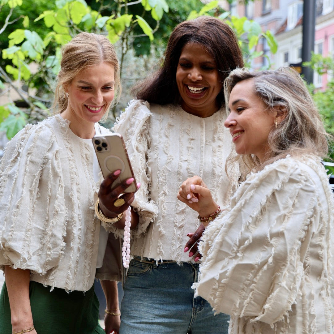 Drie vrouwen kijken lachend naar een telefoon wat zal er binnenkort gelanceerd worden